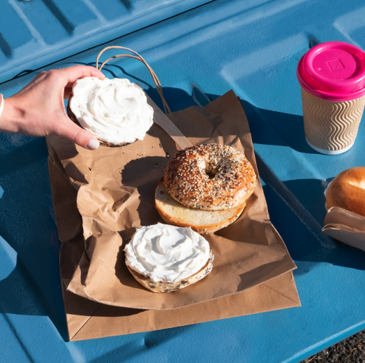 someone eating bagel and cream cheese with coffee on truck bed